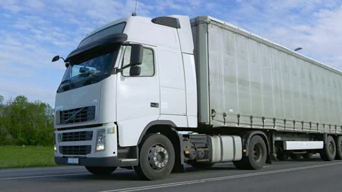 高速公路上载货拖车驾驶的超速白色半卡车。卡车是重型车辆的第一列，阳光明媚。
