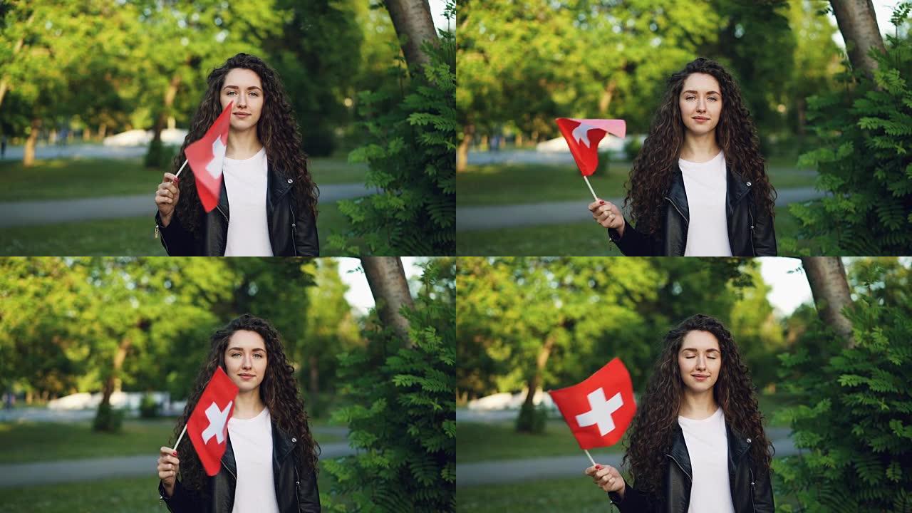 迷人的年轻女子的慢动作肖像骄傲的瑞士公民挥舞着瑞士的国旗，看着相机，微笑着。国家和民族概念。