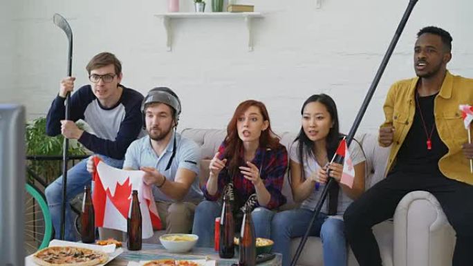 一群年轻的朋友，带着加拿大国旗的体育迷在电视上观看体育锦标赛，一起为家里最喜欢的球队加油