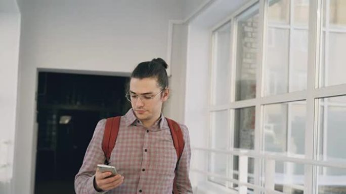 年轻英俊的高加索潮男学生正走在大学白光宽敞的走廊里，拿着电话打其他学生路过的电话