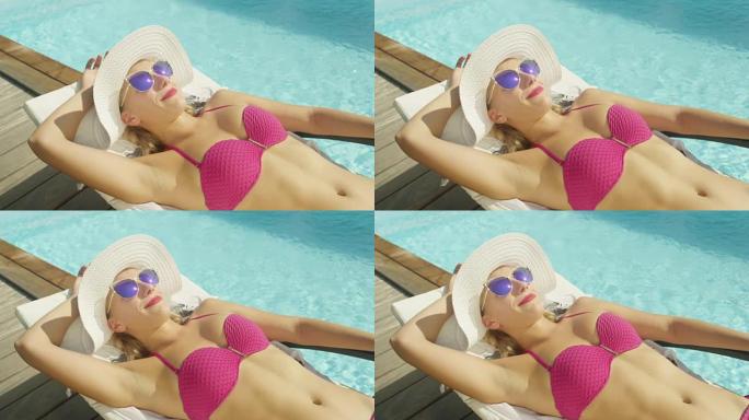 慢动作: 开朗的女人躺在游泳池旁，在夏日的阳光下晒日光浴。