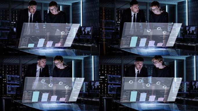 男女业务经理在充满动画屏幕的计算机的大监控室中使用触摸屏交互式3D面板。