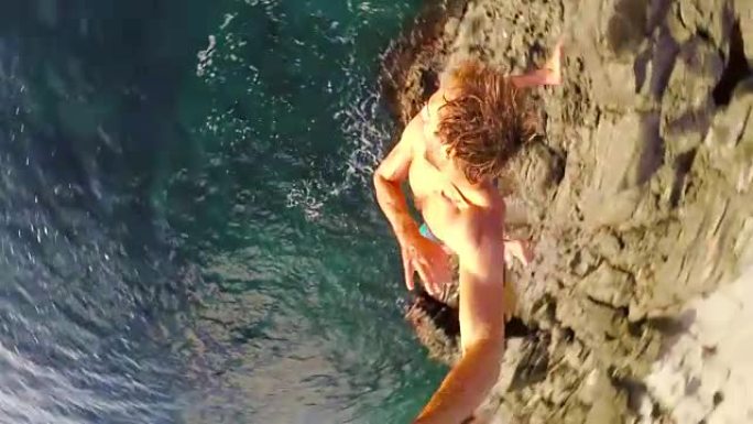 POV慢动作GOPRO自拍棒悬崖跳跃。健壮的年轻人从悬崖上跳入大海。