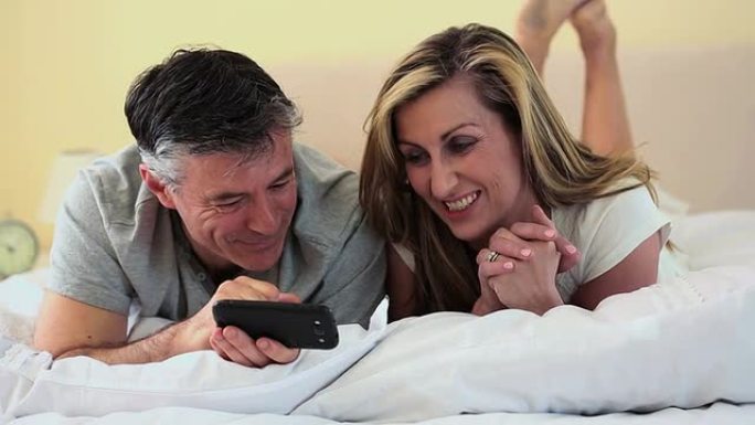 躺在床上看智能手机的成熟夫妇