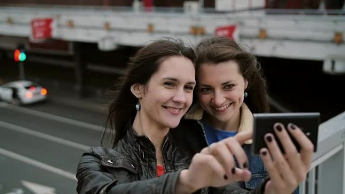 两个女孩最好的朋友自拍，站在城市的桥上，说话，微笑，大笑。慢mo