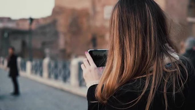 走在市中心的旅行女人，罗马广场。女性在智能手机上拍摄老城区和音乐家的照片