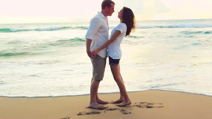 美丽的年轻夫妇在海滩日落时牵手