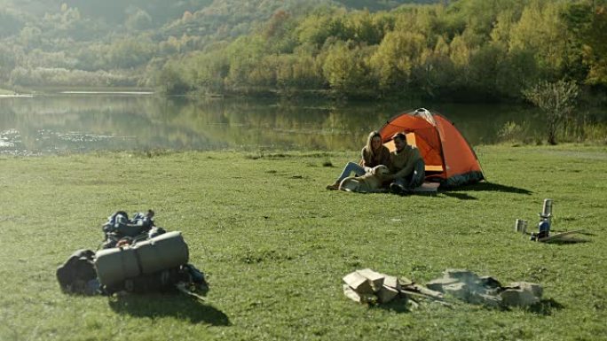 男人，女人和狗坐在湖边的帐篷前