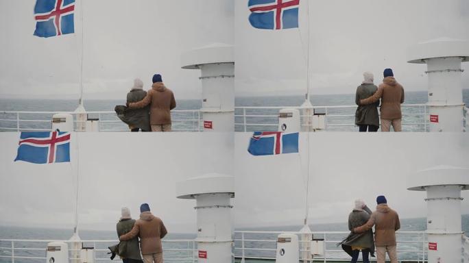 年轻时尚夫妇站在船上的冰岛国旗后视图。男人和女人在海上看