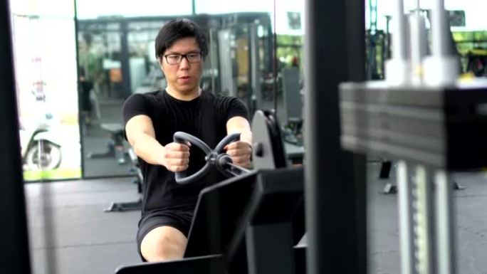 亚洲男子进行背部锻炼的手持镜头: 坐在低位的电缆排