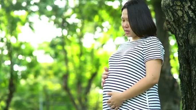 亚洲孕妇在公园摸肚子的肖像。