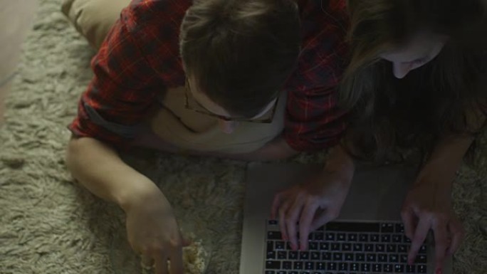 年轻夫妇躺在地板上，使用笔记本电脑。休闲生活方式。