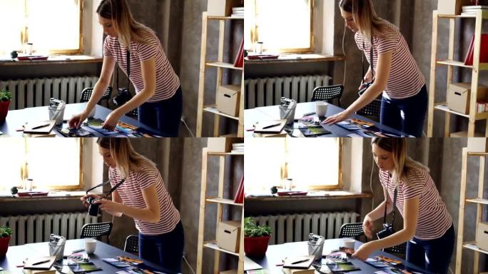 年轻的女摄影师正在用桌上五颜六色的照片平躺，并用相机拍摄。她正在桌子上的调色板和标记附近显示图片。