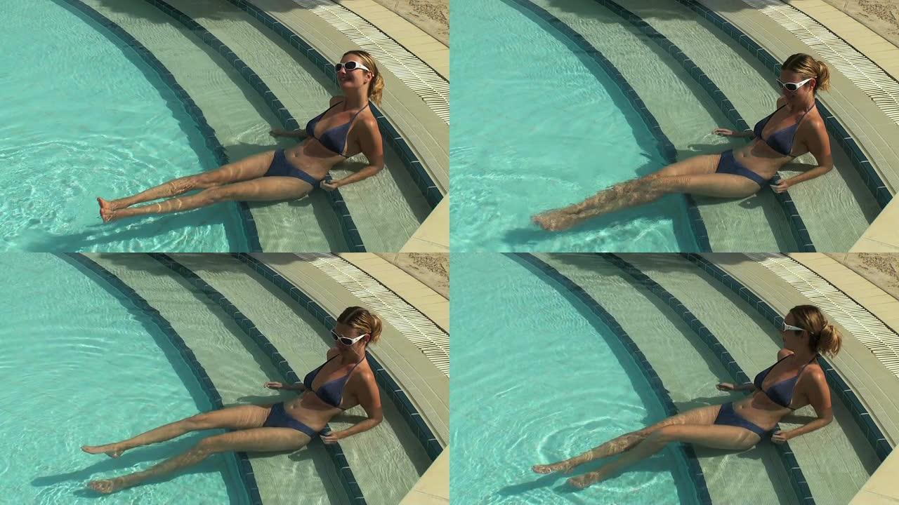 年轻女子在游泳池楼梯上放松和晒日光浴