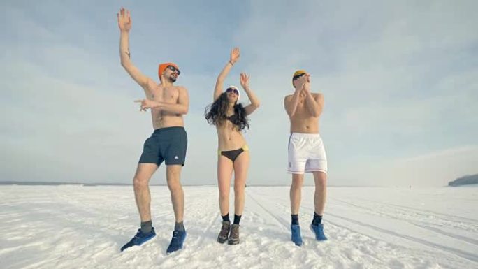 一名妇女和两名男子穿着泳装，双臂在雪地上跳舞。4K。