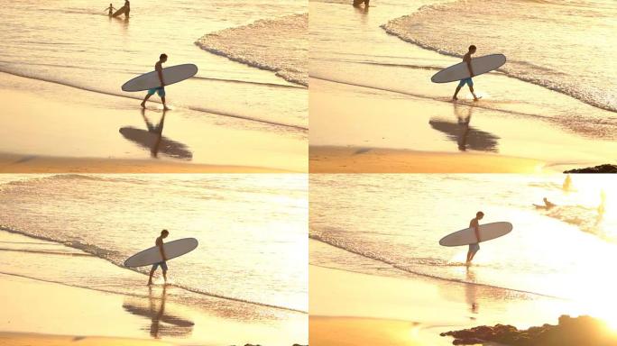 慢动作: 年轻人在金色的日落时带着冲浪板下水
