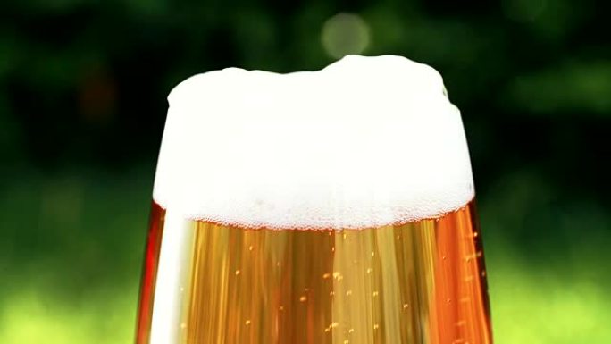 品脱玻璃杯中的冰镇啤酒在户外看起来清新，背景是绿色