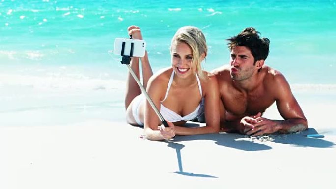 夫妇躺在海滩上，用手机拍了一张自拍