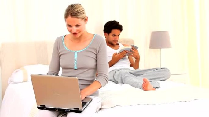 年轻的夫妇，他们的笔记本电脑和书在他们的床上