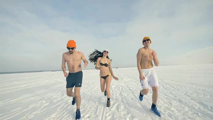三个慢跑者在冬天穿着靴子，帽子和泳衣练习。