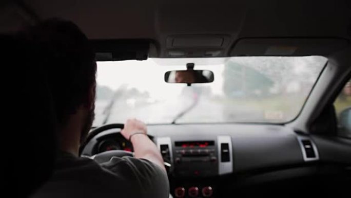 一个男人在雨中开车的背景图。手放在方向盘上，刮水器在工作