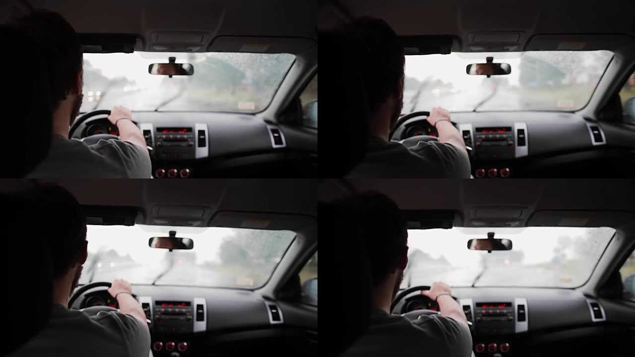 一个男人在雨中开车的背景图。手放在方向盘上，刮水器在工作
