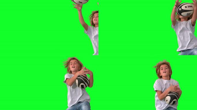 男孩在绿色屏幕上跳跃并抓住橄榄球球