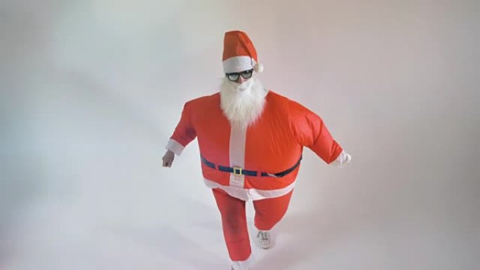 一个穿着充气圣诞老人服装的男人在白色房间里跳舞。