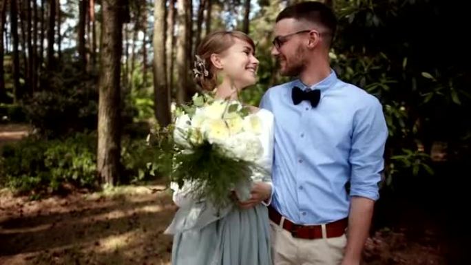 年轻美丽的一对新婚夫妇在公园里的绿树背景下亲吻