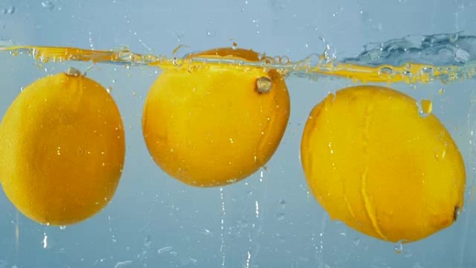三个明亮的柠檬掉进水里。