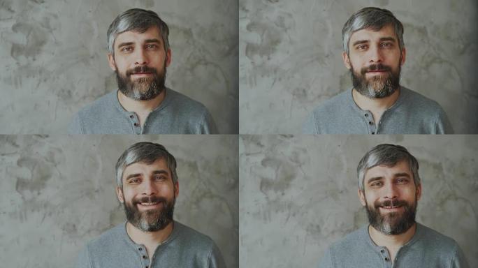 大胡子中年男子微笑并在灰色背景上看着相机的特写肖像