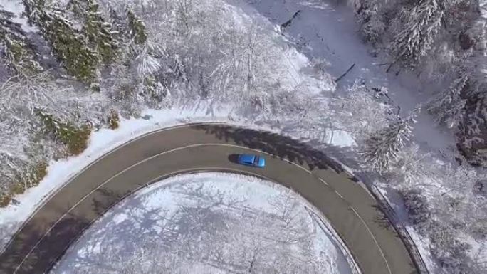 空中: 蓝色汽车在神奇的白雪皑皑的冬季仙境中行驶急转弯