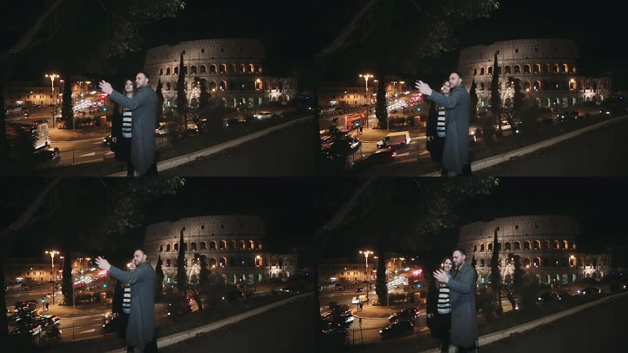 年轻美丽的夫妇站在意大利罗马竞技场附近，晚上在智能手机上聊天自拍照片