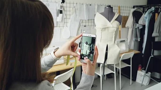 年轻的女性服装设计博客作者正在拍摄剪裁假人，上面固定着半成品服装。女孩的手和智能手机的特写镜头。