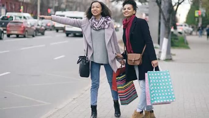 两名有吸引力的非洲裔美国妇女带着购物袋，从商场销售回来时叫出租车