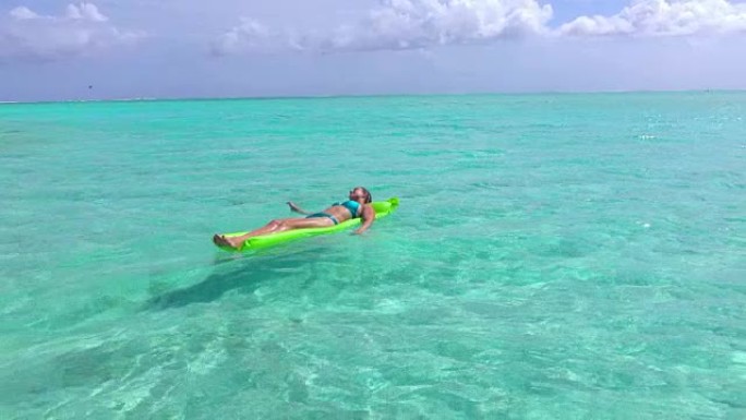 慢动作特写: 穿着泳衣的快乐年轻女子在热带岛屿的暑假里在美丽的蓝色泻湖里漂浮在充气气床床垫上放松