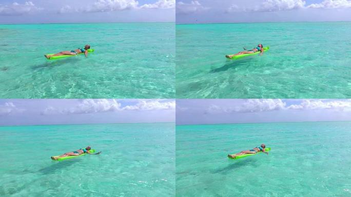 慢动作特写: 穿着泳衣的快乐年轻女子在热带岛屿的暑假里在美丽的蓝色泻湖里漂浮在充气气床床垫上放松