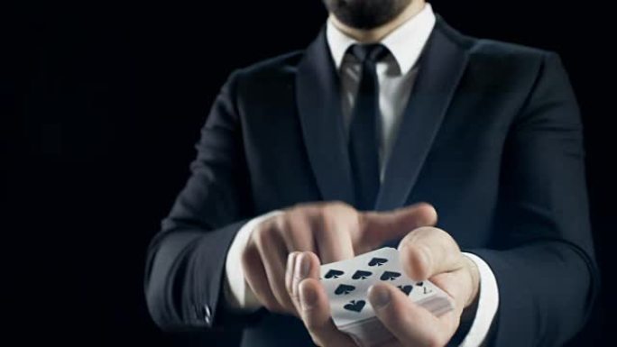 一个合适的魔术师的手的特写表演技巧，扇出卡片，用手指旋转一张卡片。背景是黑色的。