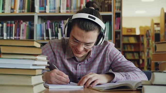 年轻英俊的白人男生坐在大学校图书馆的桌子旁，正在写一些文案。他微笑着，看起来积极快乐，书躺在桌子上