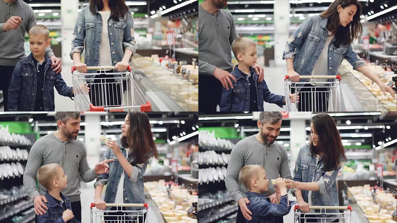 幸福的家庭在超市里选择奶酪，女人在拿一块，看着它，闻它，然后她的丈夫和儿子在闻它，放进手推车。