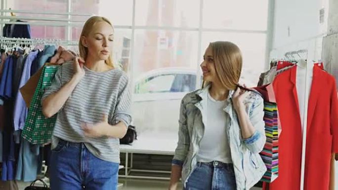 多莉拍摄的两个女孩拿着五颜六色的纸袋慢慢走过宽敞的商店。其中一个在感情上说话，另一个在倾听和微笑。