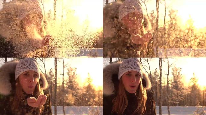 慢动作: 欢快的女孩在下雪的冬天日落时将雪花吹入相机