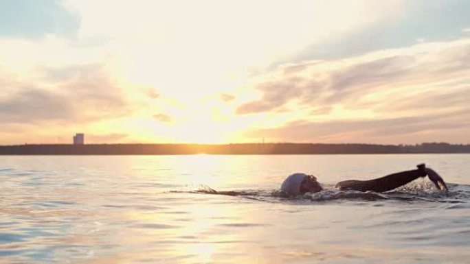 铁人三项游泳运动员在日落时在湖中练习
