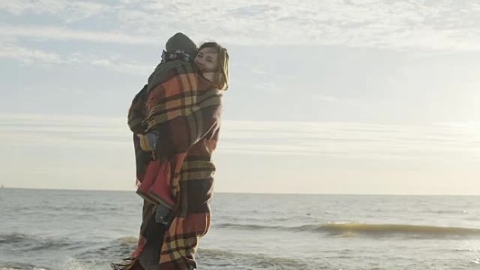 可爱的小男孩和他的母亲在海边。穿着格子的女人拥抱她的儿子并握住手。海滩上的幸福家庭