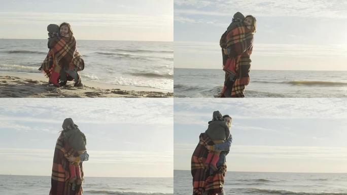 可爱的小男孩和他的母亲在海边。穿着格子的女人拥抱她的儿子并握住手。海滩上的幸福家庭