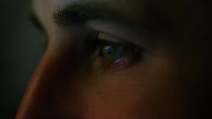 一个绿蓝男人眼睛的特写镜头，屏幕上有反射。他用不同的颜色照亮。