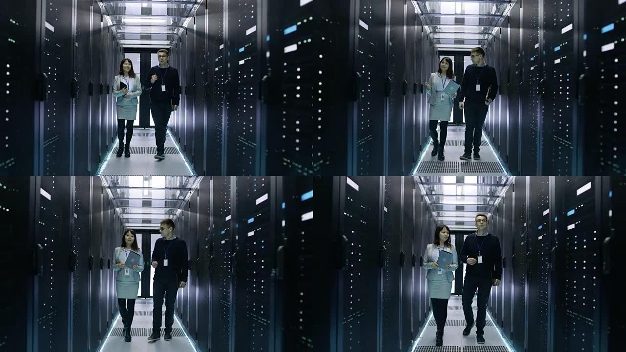 白人男性和亚洲女性IT技术人员行走在数据中心与一排排机架服务器。他们在讨论，她拿着平板电脑。