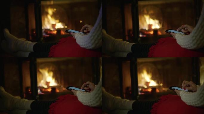4k女人放松，在舒适的壁炉旁使用智能手机，实时