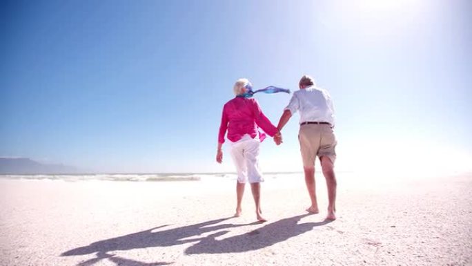 一对老年退休夫妇一起沿着海滩散步的后视图