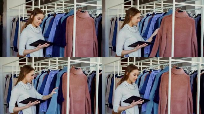 女装店的老板在使用平板电脑时正在检查和计数铁轨上的服装。她正在输入有关她的商品的信息。小企业概念。